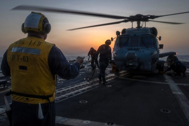A photo released by US Central Command shows a sailor directing a helicopter aboard the gu