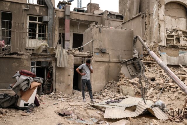 A man speaks on a mobile phone as he stands outside damaged homes, following a military st