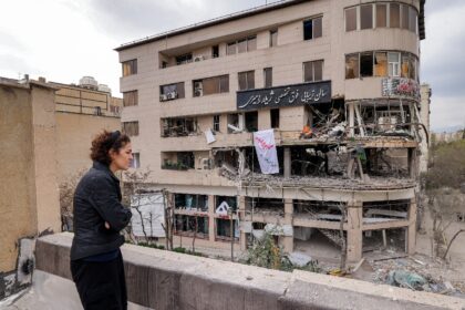 A woman standing on a rooftop in Tehran views destruction in an office building that house