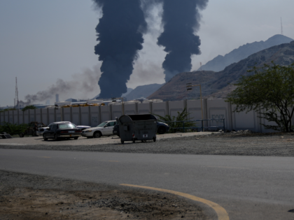FILE - A man rides a bike as fires and plumes of smoke rise after debris from an intercept