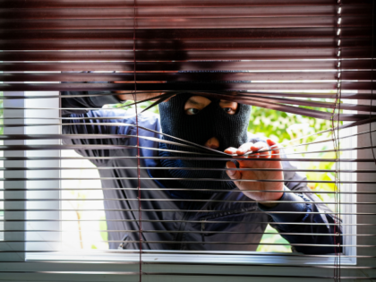 A thief in a black mask peeking through blinds