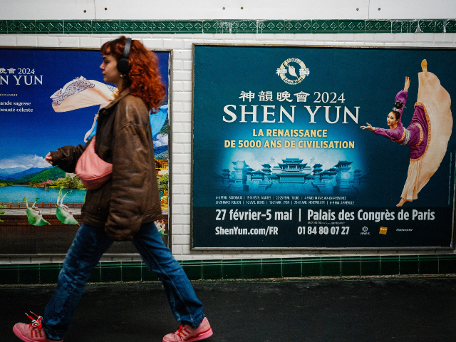 GettyImages-2068302990 This photograph taken on March 1, 2024, shows a woman walking past posters of the Shen Yun