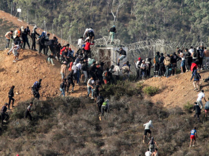 Migrants storm a barbed-wire fence as they attempt to cross the land border with Spain