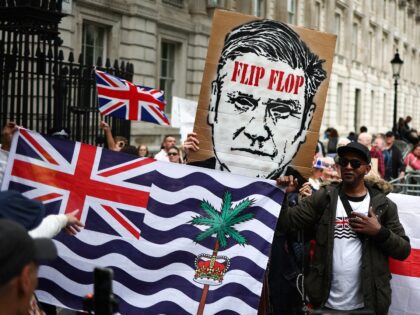 A protestor holds the flag of the British Indian Ocean Territory is font of a placard depi