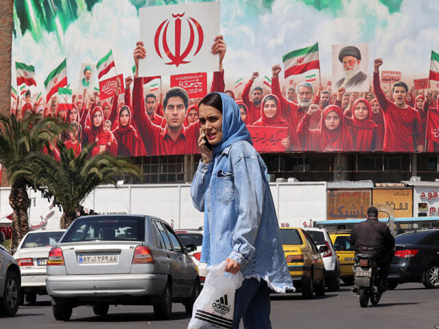 TOPSHOT - A woman crosses the road before a large political banner, depicting missiles bei