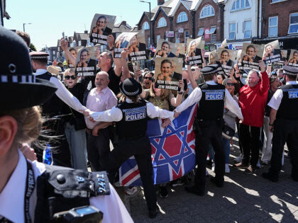 Police hold back protesters holding placards as a car (not pictured) carrying Britain'