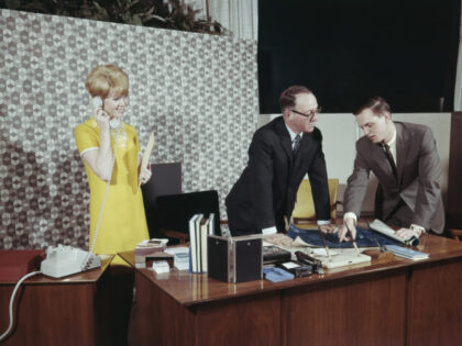 Businessmen preparing blueprint in office while assistant talking on telephone