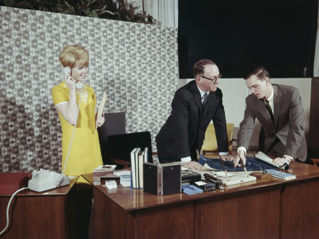 Businessmen preparing blueprint in office while assistant talking on telephone