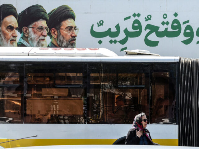 An Iranian woman walks past a bus under a banner featuring Iran's late supreme leader