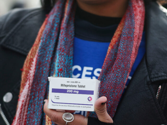 A demonstrator holds a box of mifepristone pills in front of the Supreme Court which is he