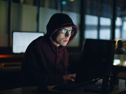 Night hacker cracking databases at evening closeup. Scammer commits fraud using AI looking