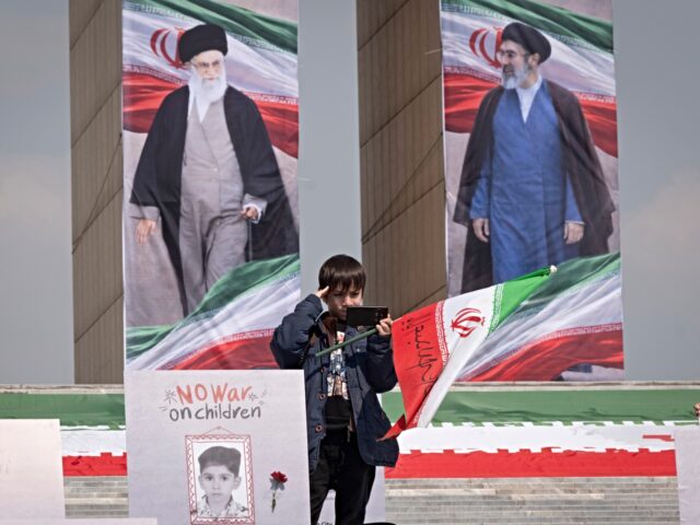An Iranian schoolboy salutes while standing beside a portrait of a child killed in an airs