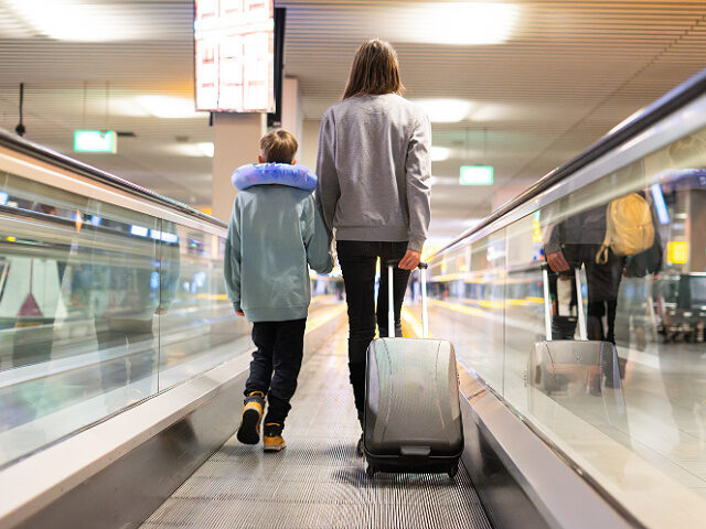Mother and child walking on airport travelator with luggage towards departure gate