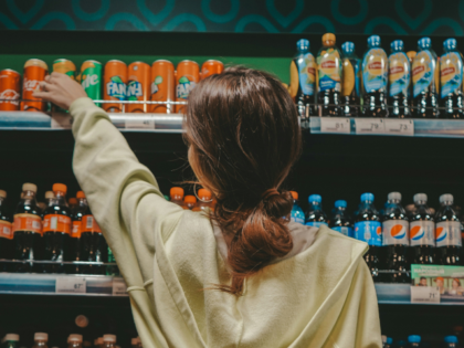 woman in beige sweater and blue denim jeans standing in front of glass soda bottles