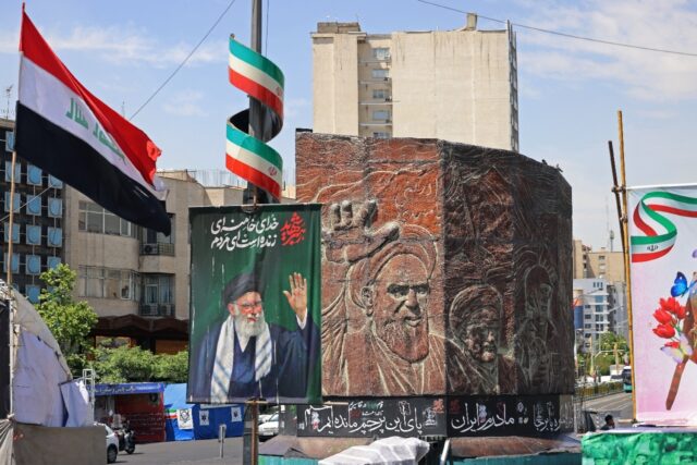 Commuters make their way past a picture of Iran's slain supreme leader Ayatollah Ali