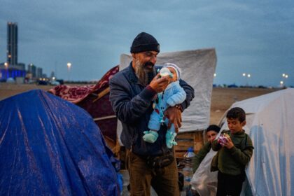 A man feeds his baby with a bottle at a make-shift camp for the displaced set up along the