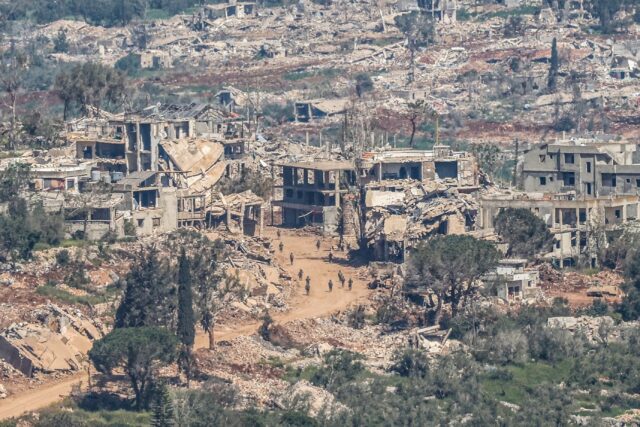 Israeli soldiers walking along the road between destroyed houses in southern Lebanon