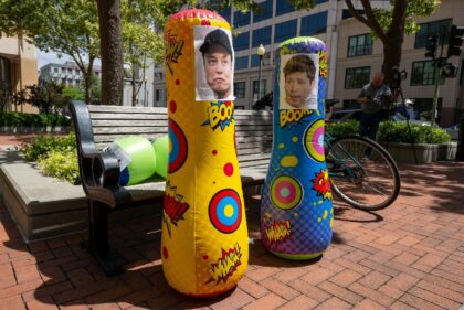 Punching bags with the faces of AI founders Elon Musk and Sam Altman are placed in front o