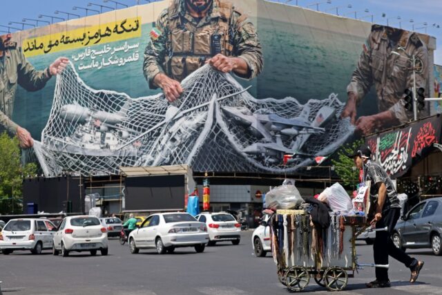 In Tehran, a vendor pushes his cart past a giant billboard reading 'The Strait of Hor