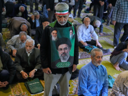 An Iranian worshipper wears a banner showing portraits of the Supreme Leader Ayatollah Moj