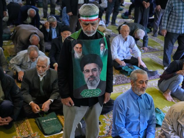 AP26114482167904 An Iranian worshipper wears a banner showing portraits of the Supreme Leader Ayatollah Moj
