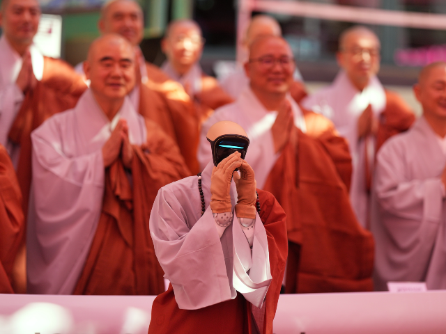 A humanoid robot, front, and Buddhist monks put hands together for a photo after an ordina