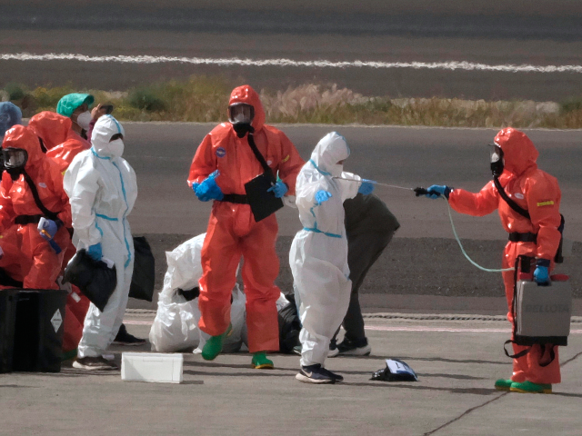 Passengers are sprayed with disinfectant by Spanish government officials before boarding a