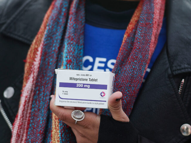 A demonstrator holds a box of mifepristone pills in front of the Supreme Court which is he