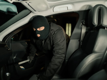 Thief Using Crowbar To Open Car's Door.Auto thief in black balaclava trying to break