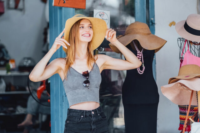 Smiling woman trying on sun hat at outdoor second-hand store.