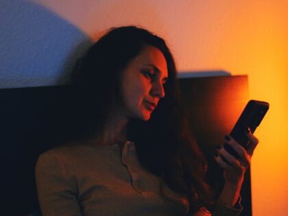 A contemplative moment of a young woman sitting in a dimly lit room, browsing her smartpho