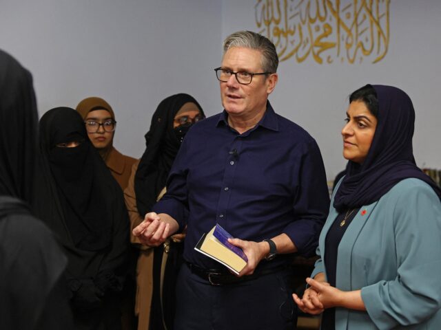 Britain's Prime Minister Keir Starmer holds a copy of The Majestic Quran, as he stands wit