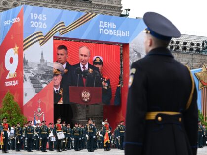 Members of a military band stand next to a screen broadcasting Russia's President Vladimir