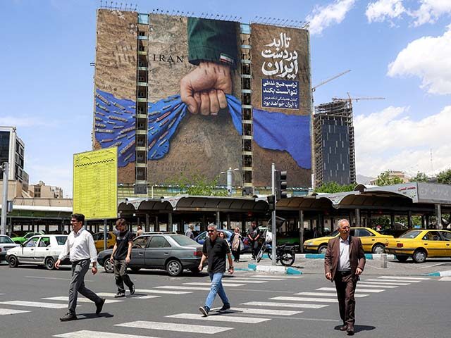 People cross a street near a billboard on the facade of a building depicting the Strait of