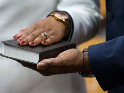 Teneshia Hudspeth places her hand on a Bible, held by her husband, Samson Babalola, as she