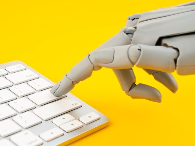 Robotic hand pressing on keyboard computer on yellow background.