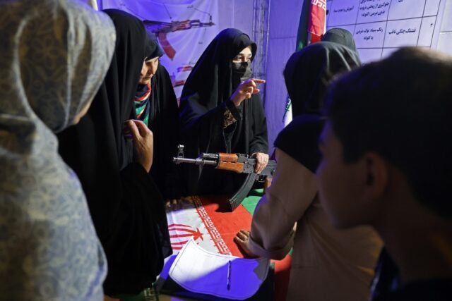 An Iranian military personnel (C) educates women about how to use a gun at a booth in Haft