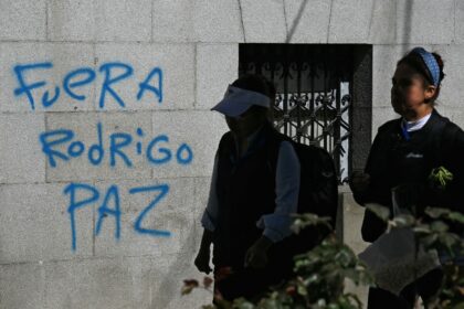 Bolivian women walk past graffiti reading 'Rodrigo Paz out,' referring to the co