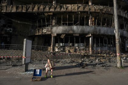 A boy plays the accordion in front of a shopping center damaged by Russian strikes in Kyiv