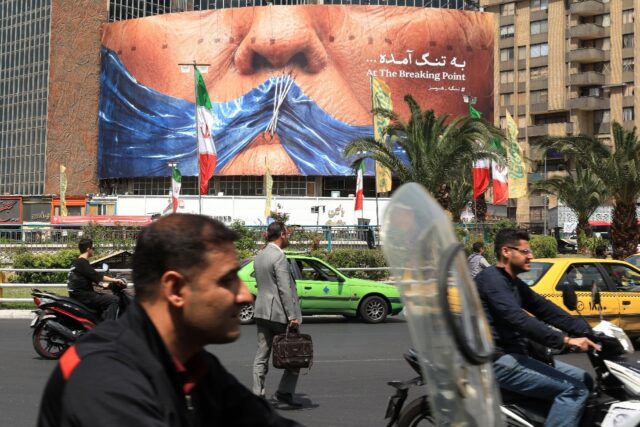 Commuters make their way past an anti-US billboard referring to President Donald Trump and