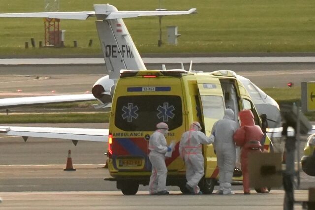 A person in a hazmat suit (2R) is escorted to an ambulance at Schiphol airport near Amster
