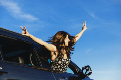 Carefree woman leaning out from car window with arms outstretched
