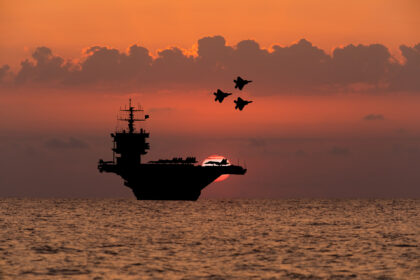 Aircraft carrier and fighters at sunset in the sea