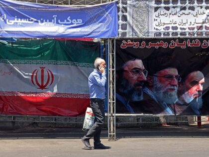 TOPSHOT - A man walks past Iran's national flag and a banner bearing the images of the lat