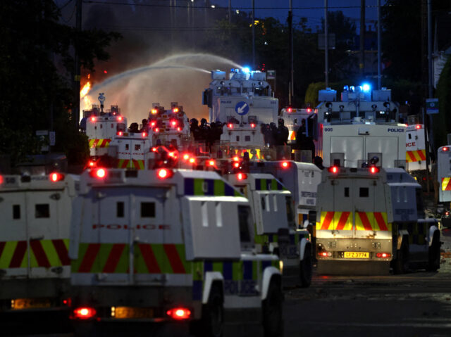 Police use a water cannon as they block the road from protesters (behind) leading to a hot