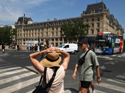 A visitor holds onto her sun hat during high temperatures in central Paris, France, on Fri