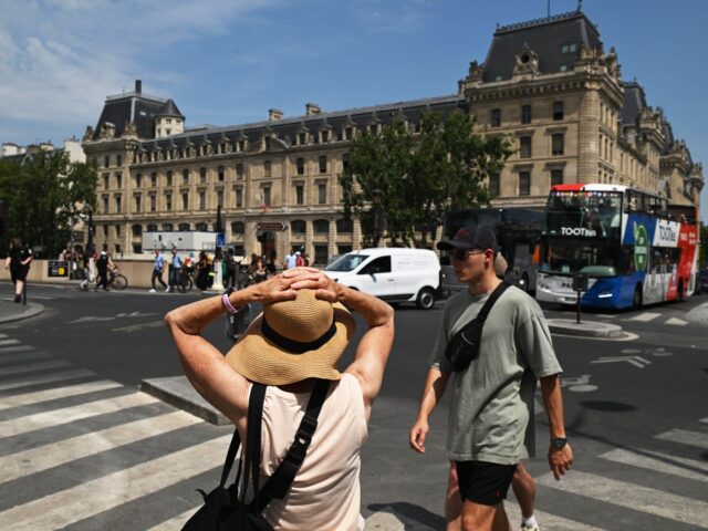 A visitor holds onto her sun hat during high temperatures in central Paris, France, on Fri