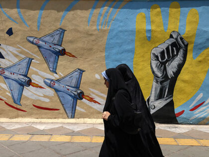Iranian women walk past an anti-US and anti-Israeli mural in Tehran on June 3, 2026. The m