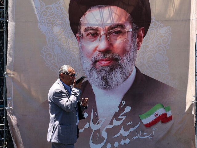 An Iranian man walks past a banner depicting Iranian supreme leader Mojtaba Khamenei at Va