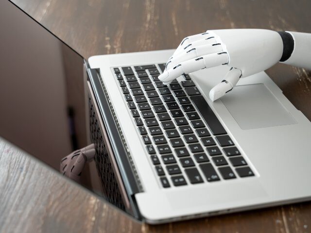 Robot hand typing on laptop keyboard on desk, futuristic AI and technology
